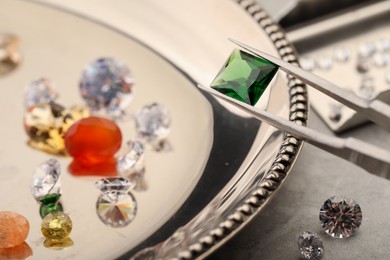 Photo of Tweezers with beautiful gemstones on light table, selective focus