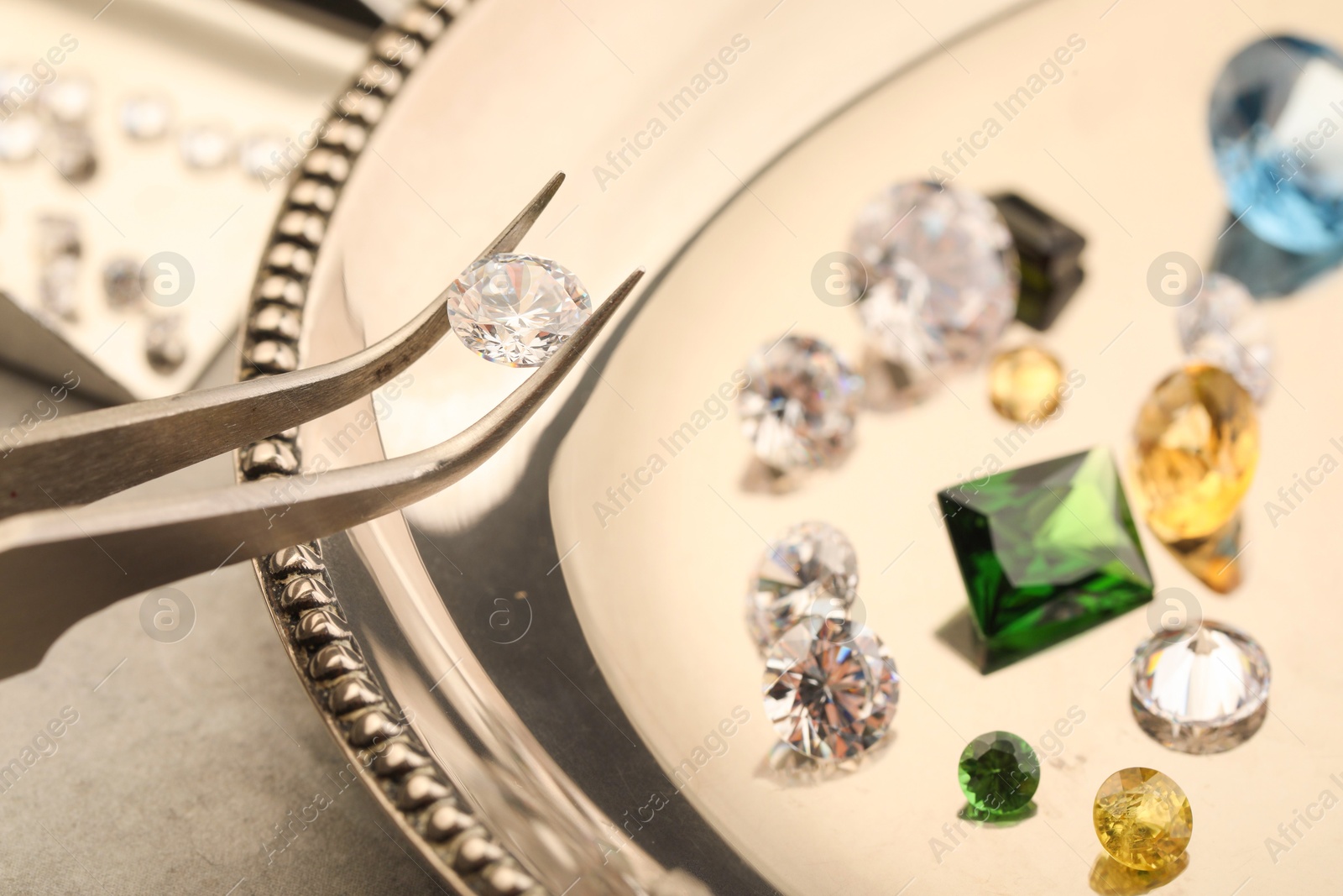 Photo of Tweezers with beautiful gemstones on light table, selective focus