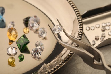 Photo of Tweezers with beautiful gemstones on light table, selective focus