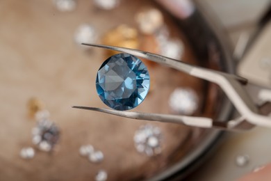 Photo of Tweezers with beautiful gemstone on blurred background, closeup