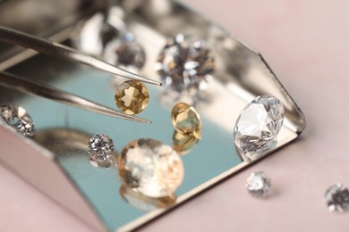 Photo of Tweezers with beautiful gemstones on light pink table, selective focus