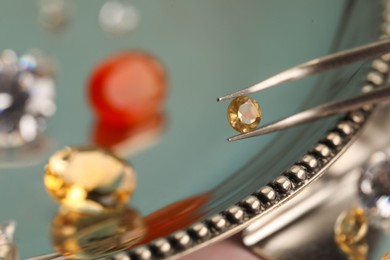 Photo of Tweezers with beautiful gemstone on blurred background, closeup