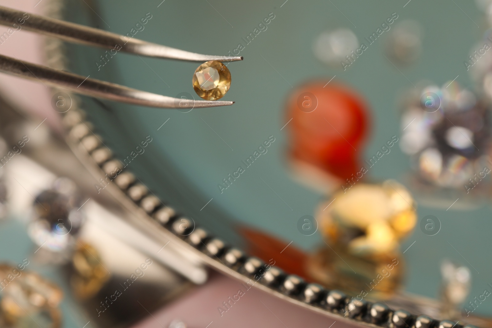 Photo of Tweezers with beautiful gemstone on blurred background, closeup