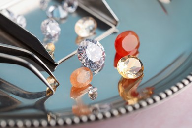 Photo of Tray with beautiful gemstones and tweezers on light pink table, closeup