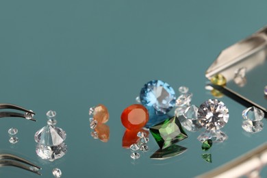 Photo of Beautiful colorful gemstones and tweezers on mirror surface, closeup