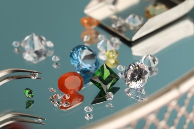 Photo of Beautiful colorful gemstones and tweezers on mirror surface, closeup