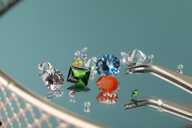 Photo of Beautiful colorful gemstones and tweezers on mirror surface, closeup