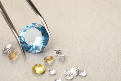 Photo of Tweezers with beautiful gemstones on light textured table, closeup. Space for text