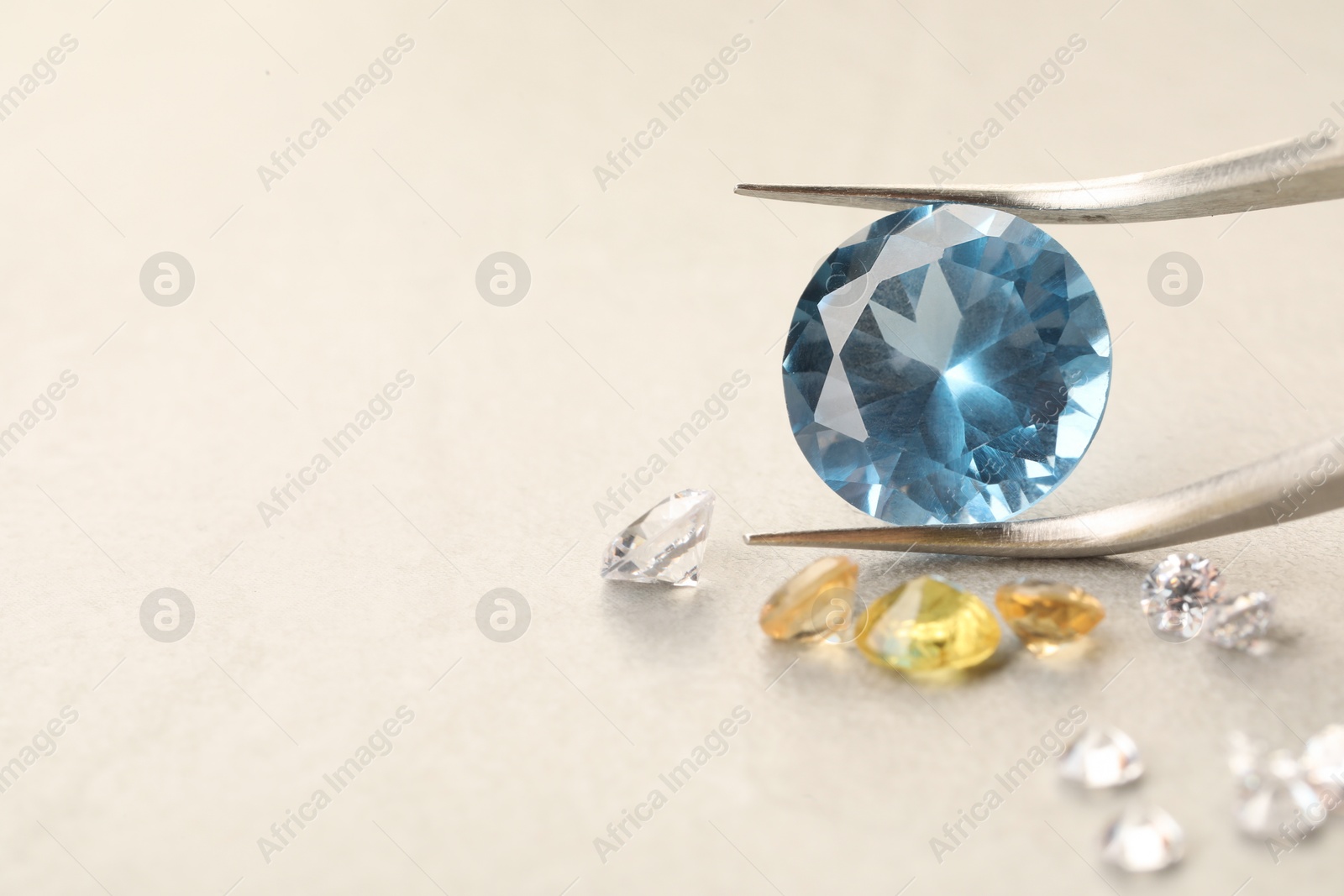 Photo of Tweezers with beautiful gemstones on light textured table, closeup. Space for text