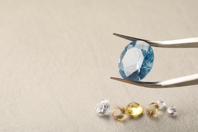 Photo of Tweezers with beautiful gemstones on light textured table, closeup. Space for text