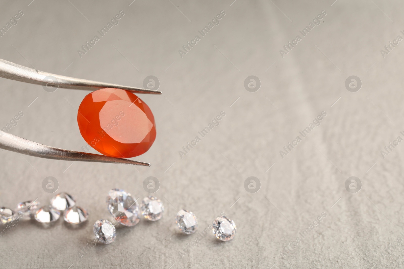 Photo of Tweezers with beautiful gemstones on light textured table, closeup. Space for text