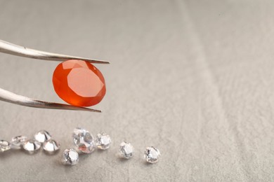 Photo of Tweezers with beautiful gemstones on light textured table, closeup. Space for text