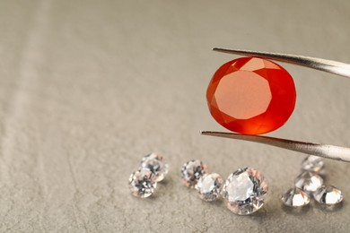 Photo of Tweezers with beautiful gemstones on textured table, closeup. Space for text