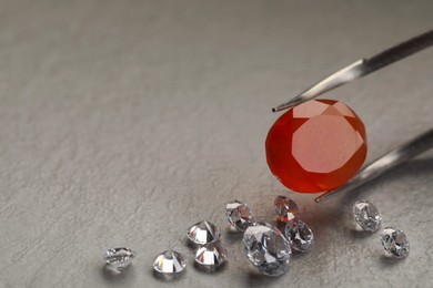 Photo of Tweezers with beautiful gemstones on textured table, closeup. Space for text