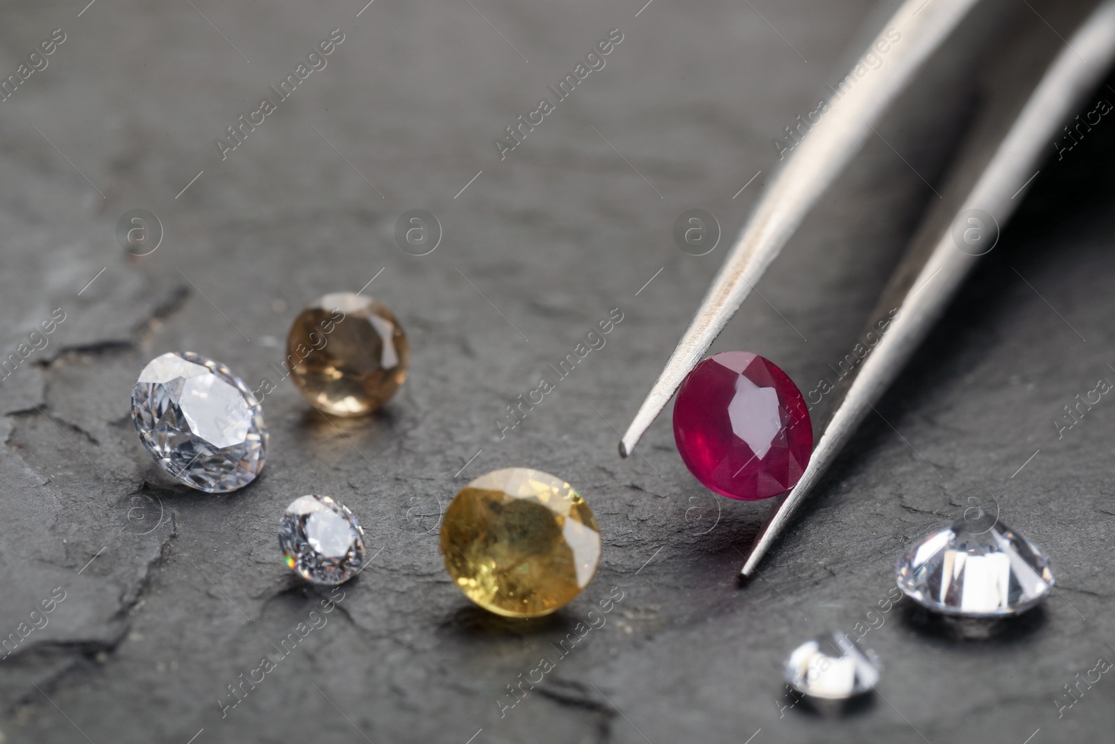 Photo of Tweezers with beautiful gemstones on grey textured table, closeup