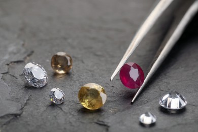 Photo of Tweezers with beautiful gemstones on grey textured table, closeup