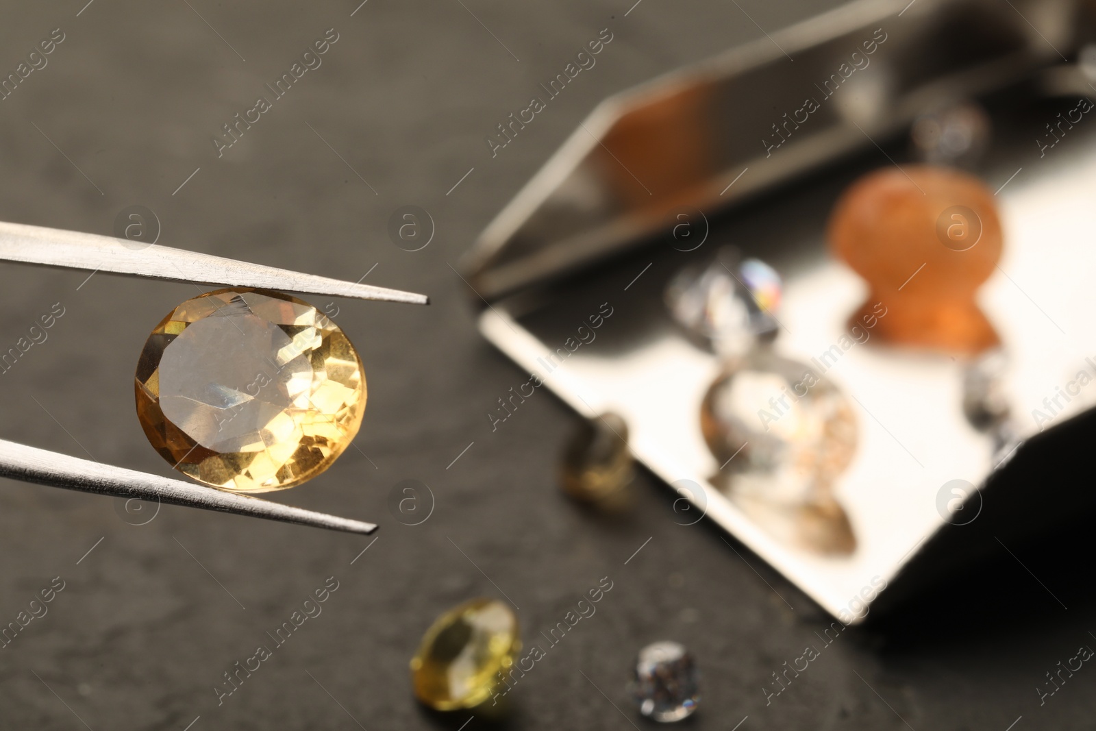 Photo of Tweezers with beautiful gemstone on blurred background, closeup