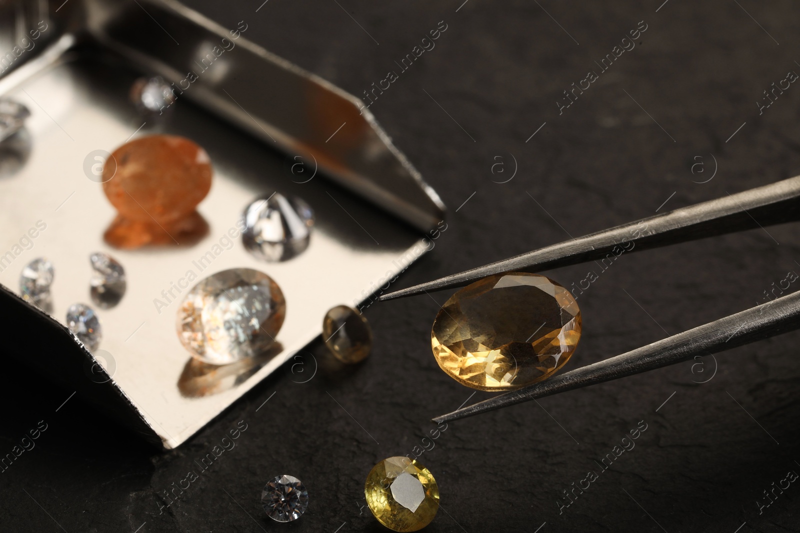 Photo of Tweezers with beautiful gemstones on black table, selective focus