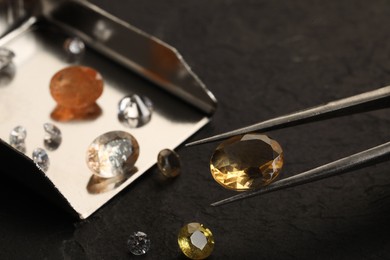 Photo of Tweezers with beautiful gemstones on black table, selective focus