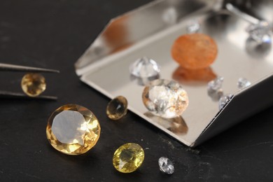 Photo of Tweezers with beautiful gemstones on black table, selective focus