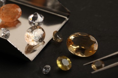 Photo of Tweezers with beautiful gemstones on black table, selective focus