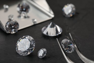 Photo of Tweezers with beautiful gemstones on black table, selective focus