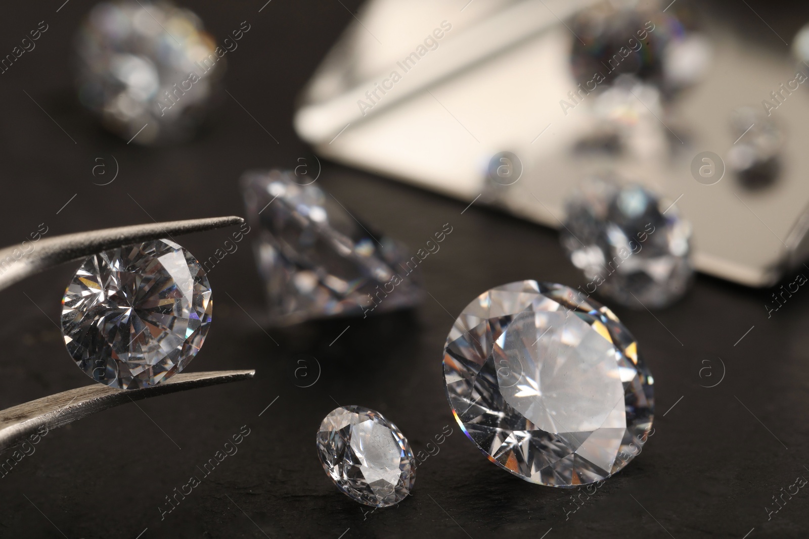 Photo of Tweezers with beautiful gemstones on black table, selective focus