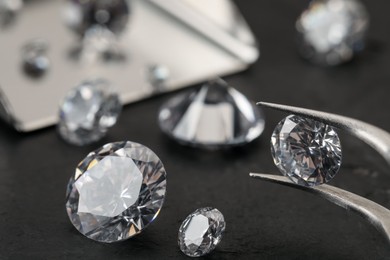 Photo of Tweezers with beautiful gemstones on black table, selective focus