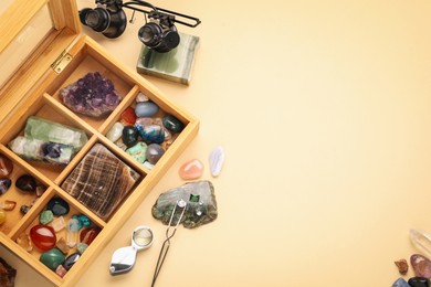 Photo of Box with beautiful gemstones and jeweler's tools on beige background, flat lay. Space for text