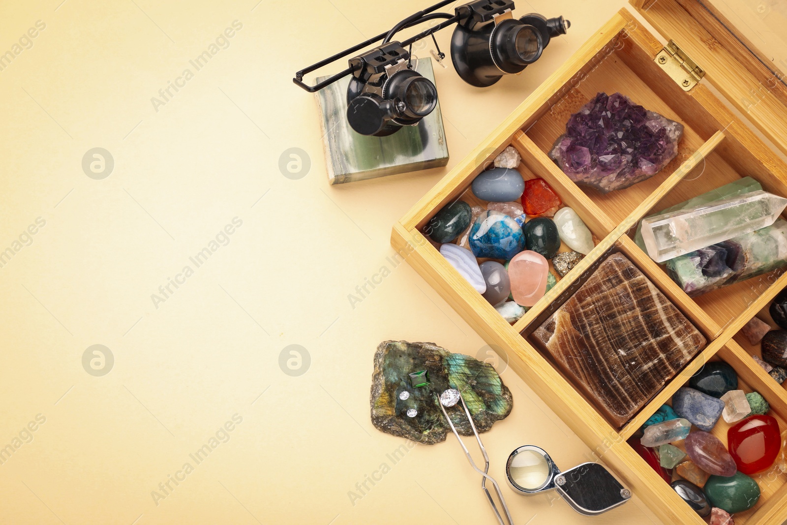 Photo of Box with beautiful gemstones and jeweler's tools on beige background, flat lay. Space for text