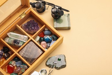 Photo of Box with beautiful gemstones and jeweler's tools on beige background, above view. Space for text