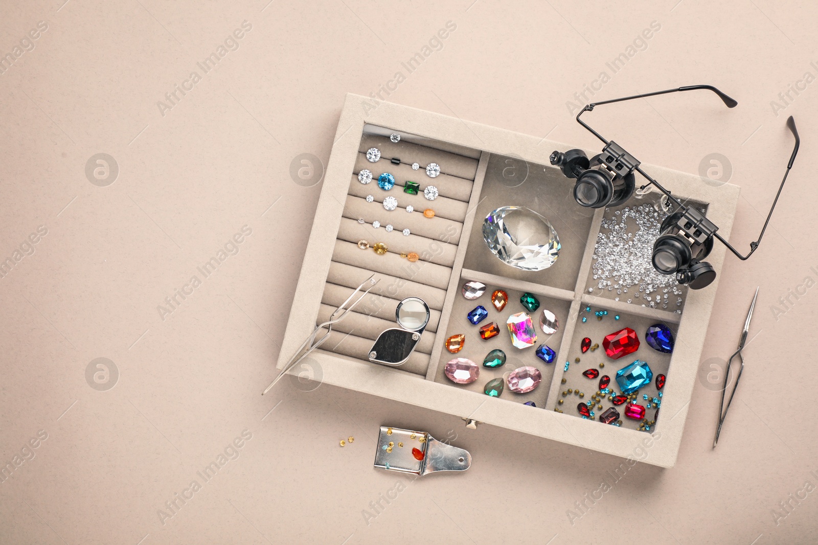 Photo of Box with beautiful gemstones and jeweler's tools on light background, top view. Space for text