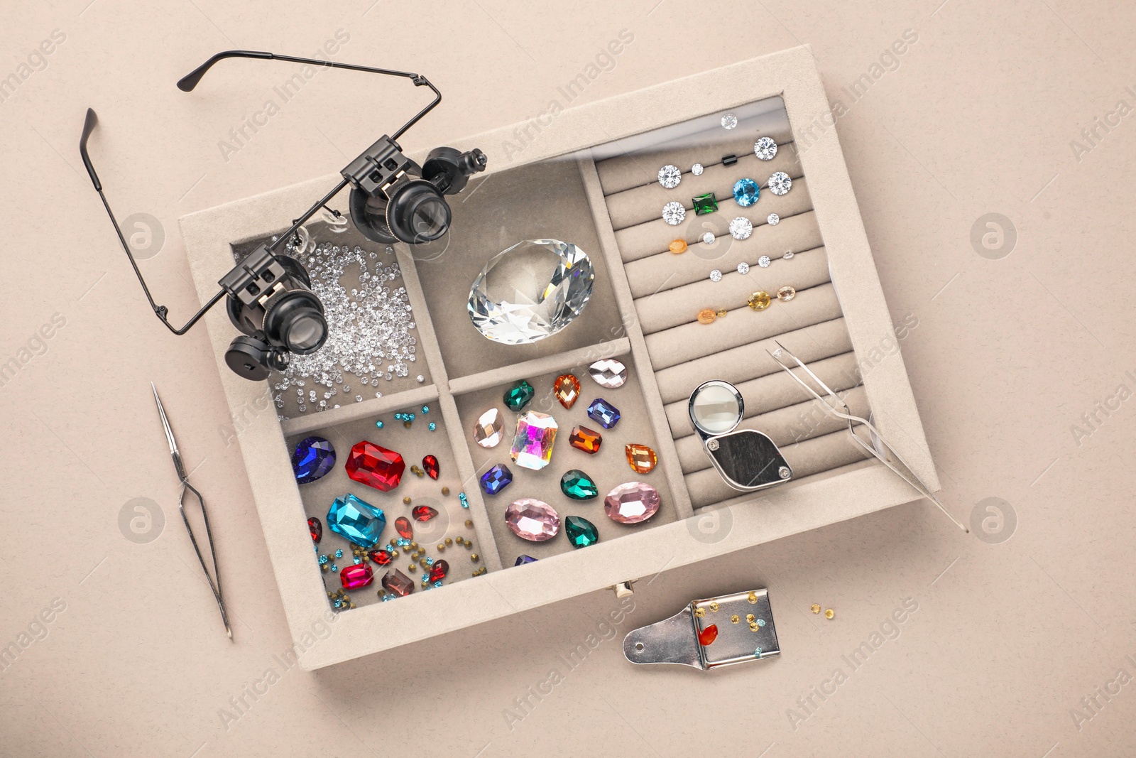 Photo of Box with beautiful gemstones and jeweler's tools on light background, top view