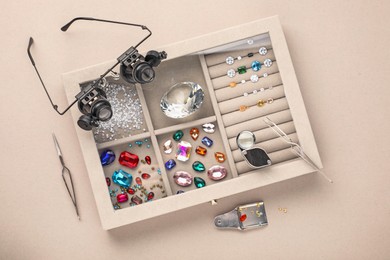 Photo of Box with beautiful gemstones and jeweler's tools on light background, top view