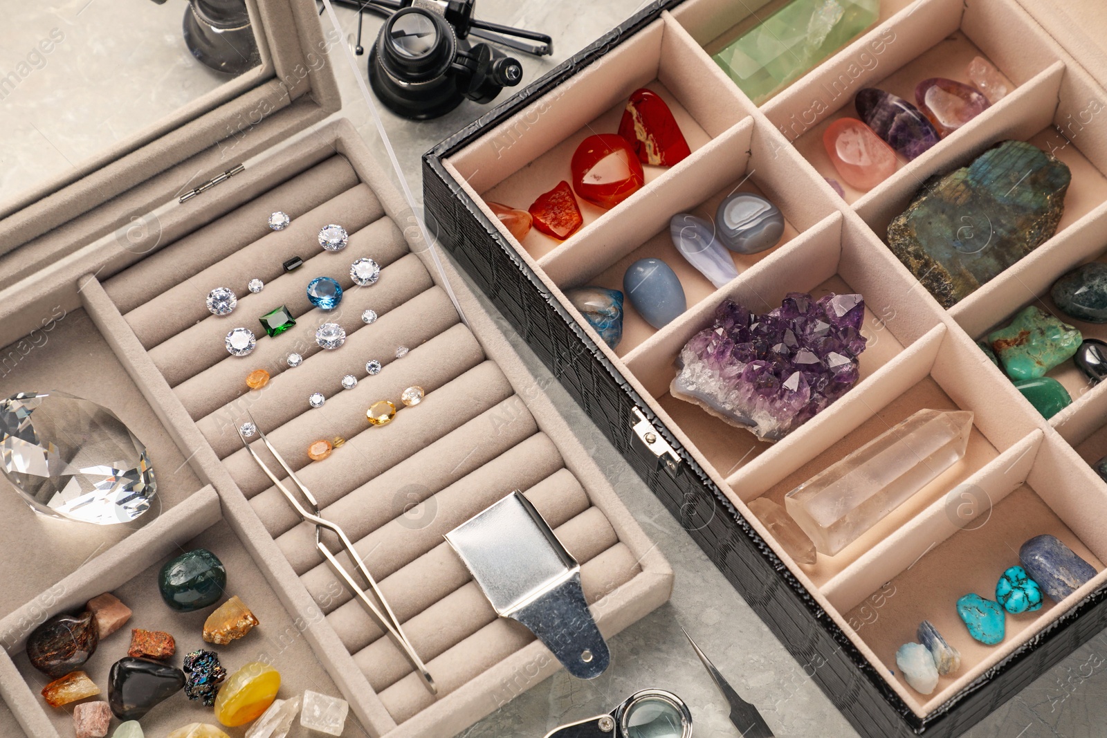 Photo of Box with beautiful gemstones and jeweler's tools on light table, closeup