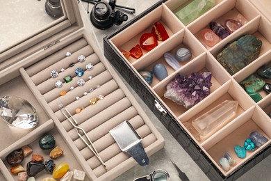 Photo of Box with beautiful gemstones and jeweler's tools on light table, closeup