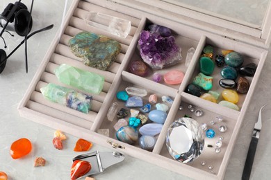 Photo of Box with beautiful gemstones and jeweler's tools on light table, closeup