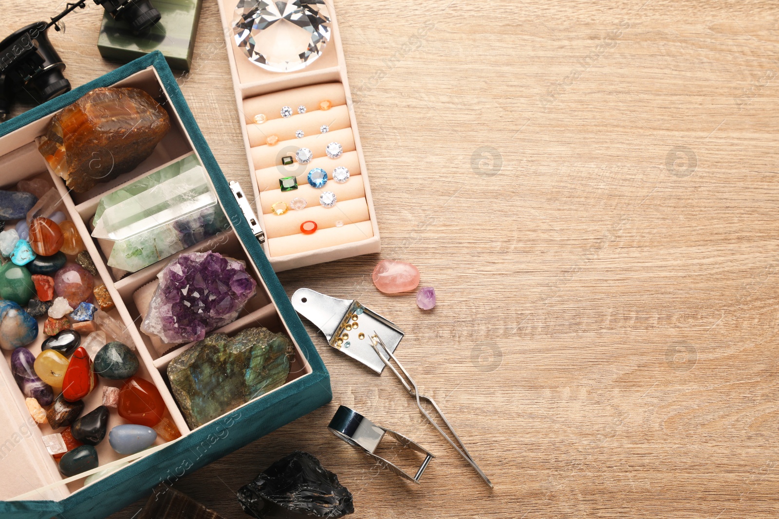 Photo of Box with beautiful gemstones and jeweler's tools on wooden table, above view. Space for text