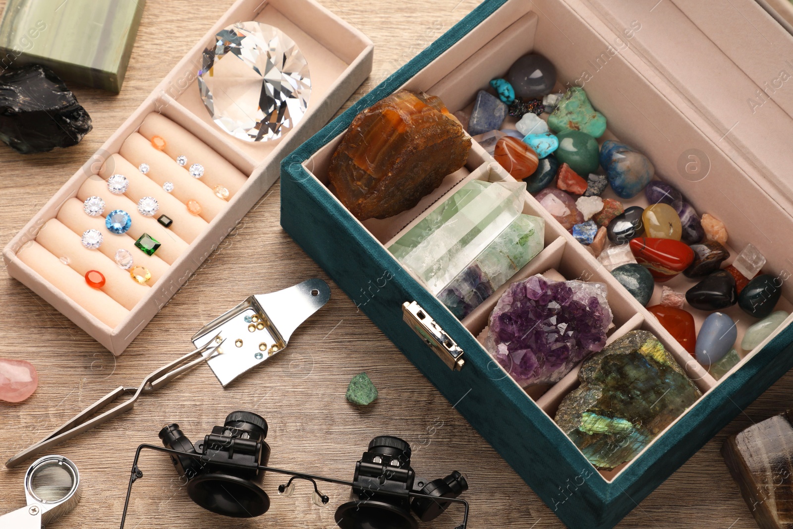 Photo of Box with beautiful gemstones and jeweler's tools on wooden table, closeup