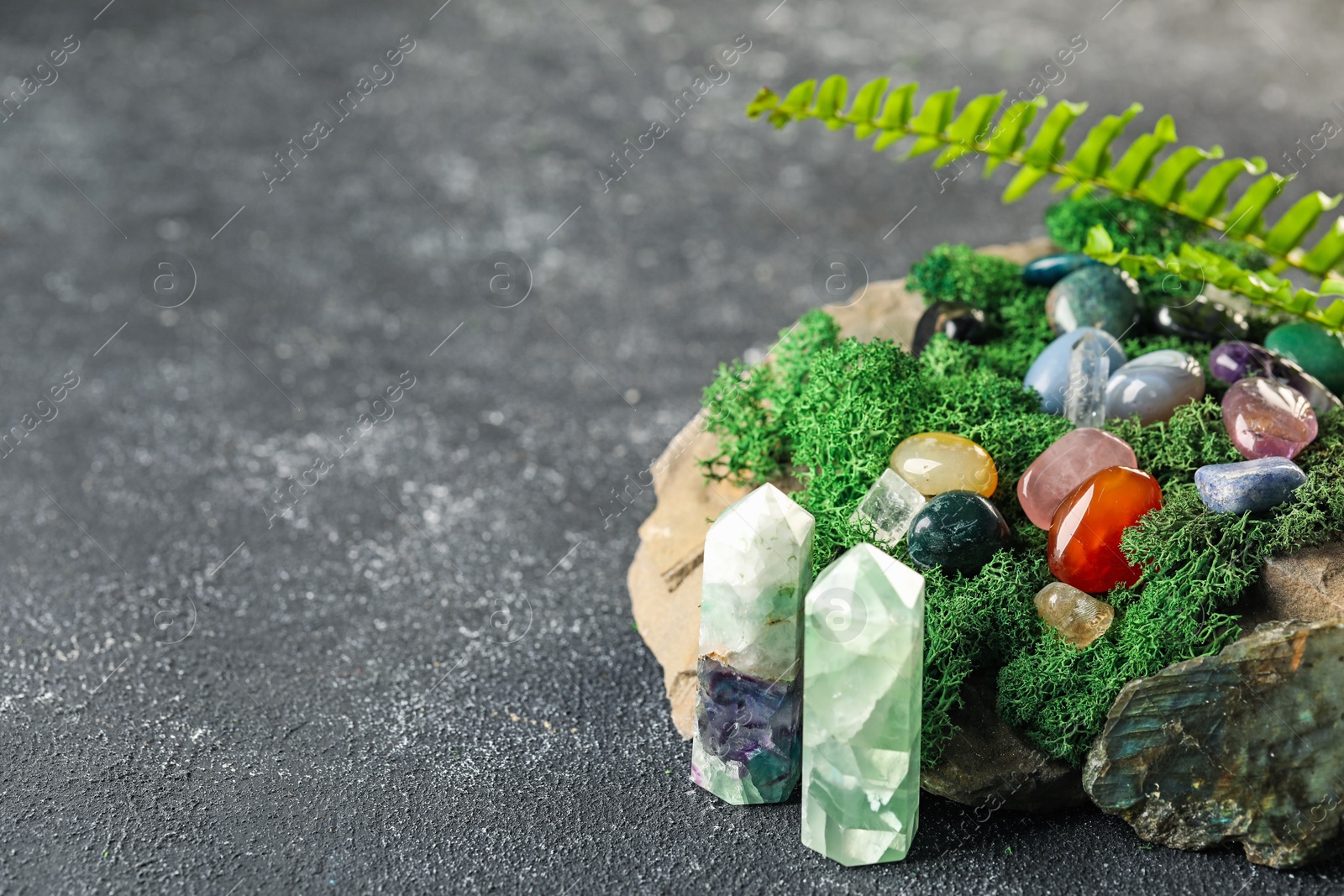 Photo of Different natural gemstones and moss on grey textured table. Space for text