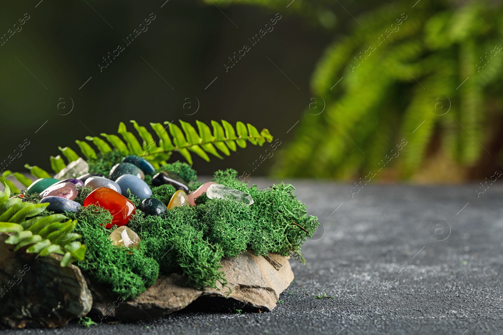 Photo of Different natural gemstones and moss on grey textured table. Space for text