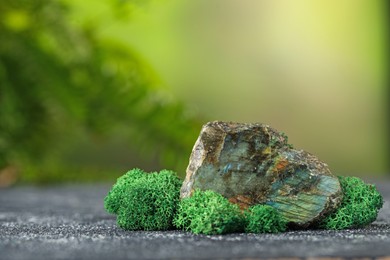 Photo of Big natural gemstone and moss on grey textured table. Space for text