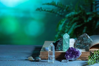 Photo of Beautiful natural gemstones and book on grey table against green background. Space for text