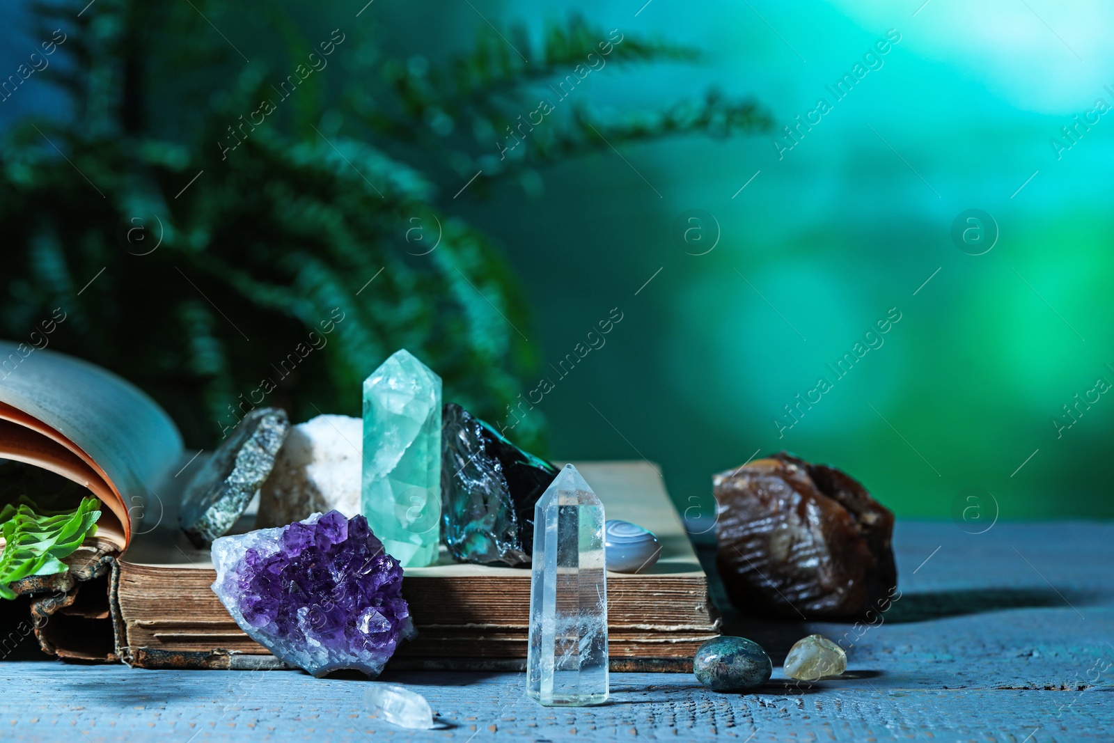 Photo of Beautiful natural gemstones and book on grey table against green background. Space for text