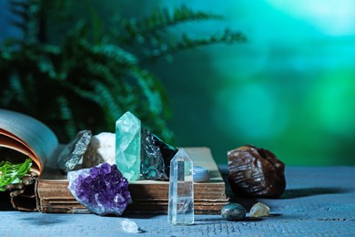 Photo of Beautiful natural gemstones and book on grey table against green background. Space for text