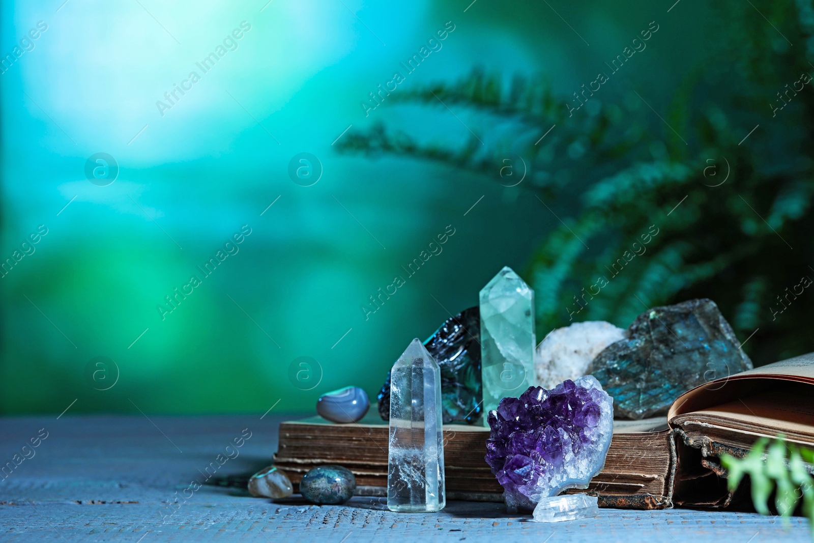 Photo of Beautiful natural gemstones and book on grey table against green background. Space for text