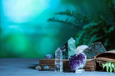 Photo of Beautiful natural gemstones and book on grey table against green background. Space for text