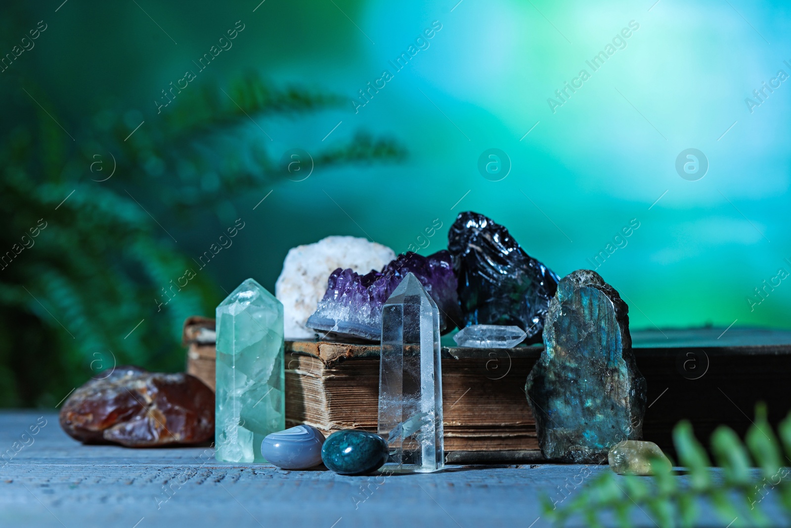 Photo of Beautiful natural gemstones and book on grey table against green background