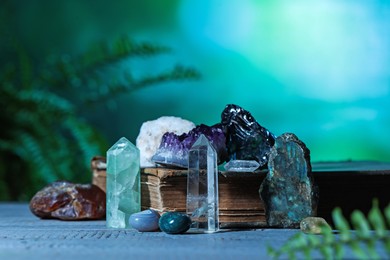 Photo of Beautiful natural gemstones and book on grey table against green background