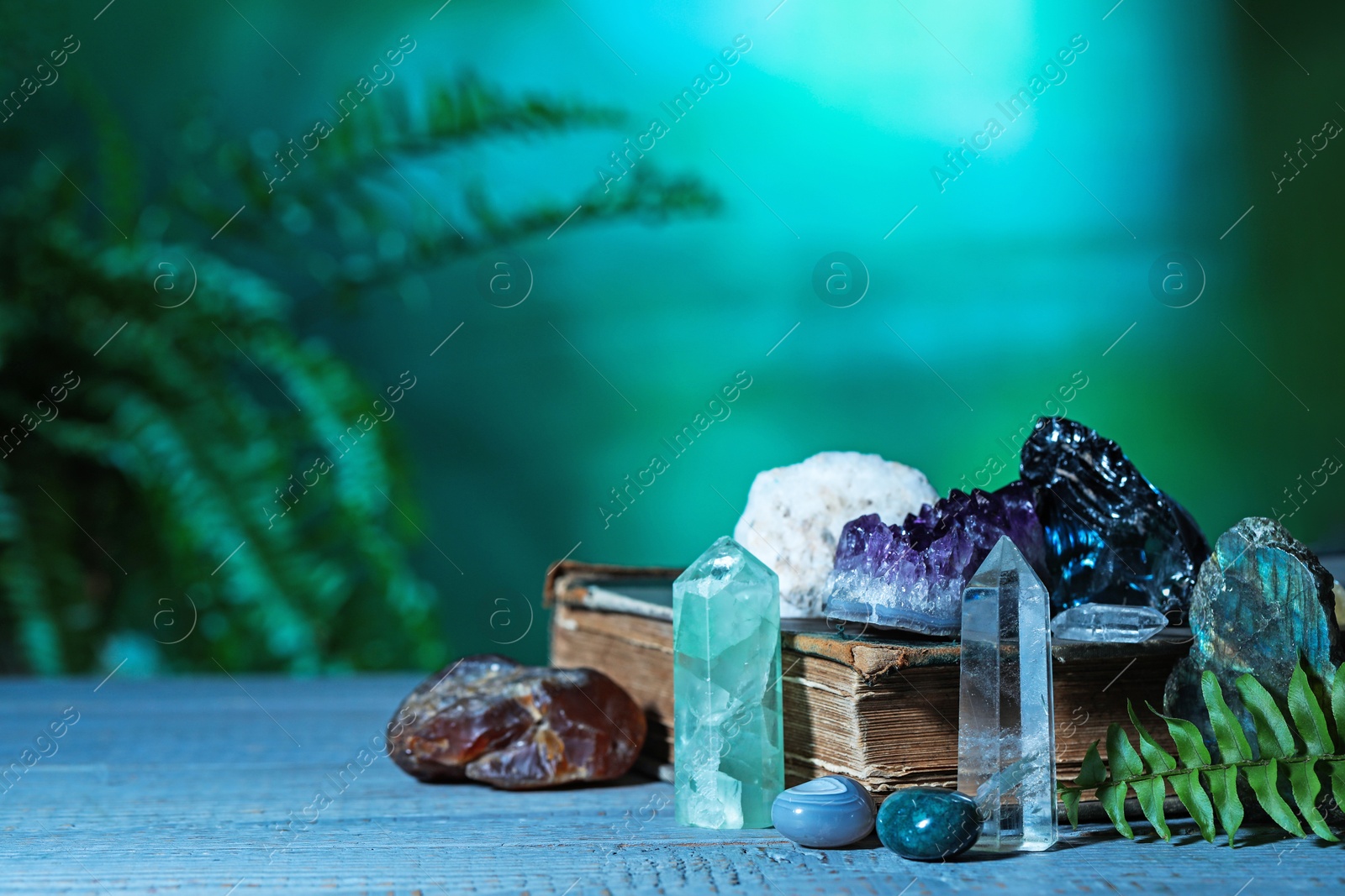 Photo of Beautiful natural gemstones and book on grey table against green background. Space for text